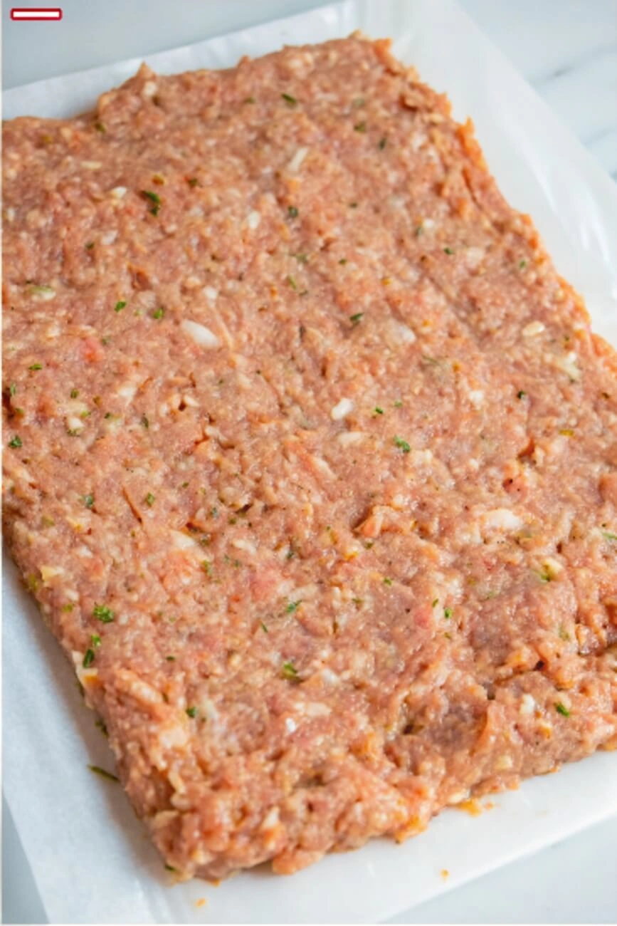Raw seasoned ground chicken mixture flattened on parchment paper