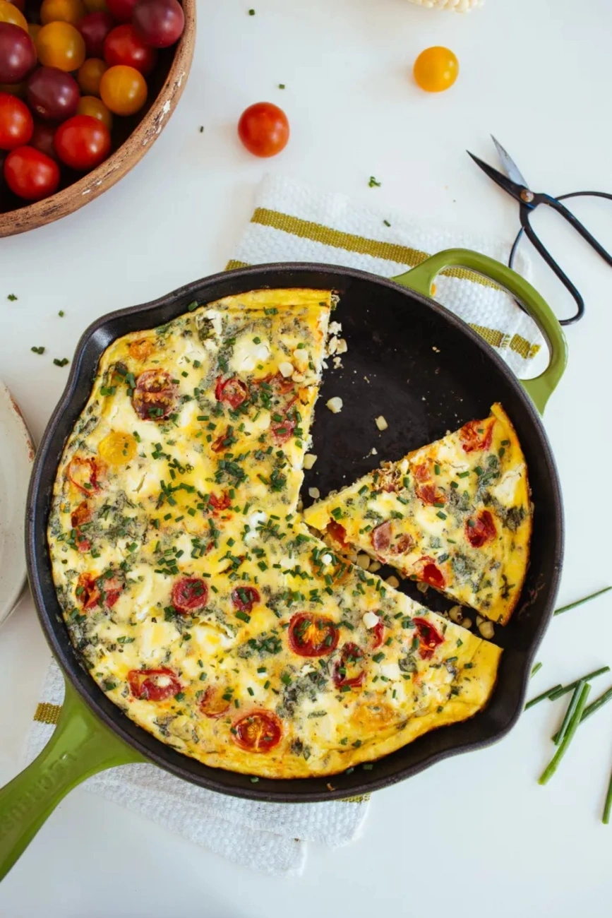 Colorful tomato and herb frittata baked in a cast iron skillet with a slice cut out.