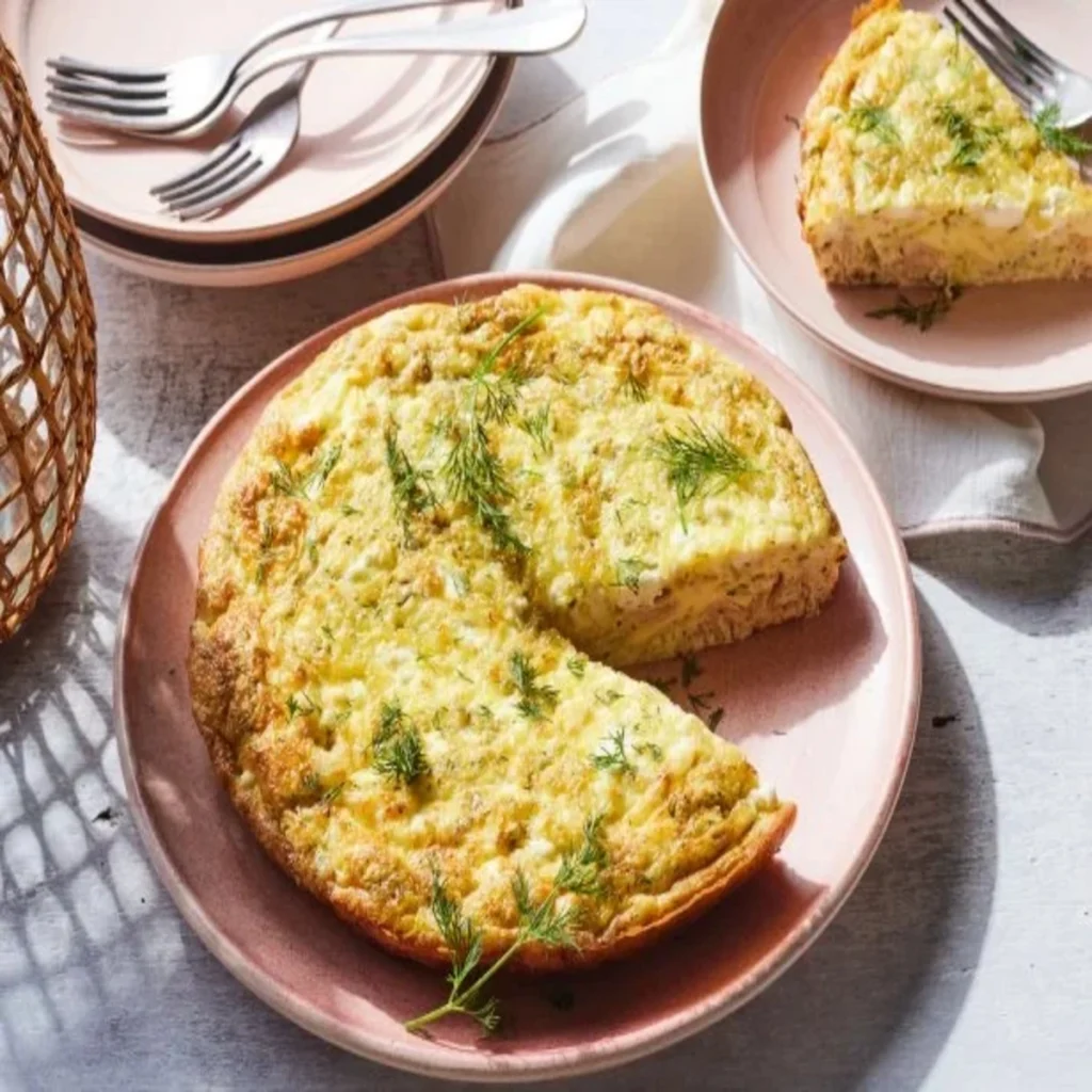 Crustless quiche topped with fresh dill, served on a pink plate with a slice removed.