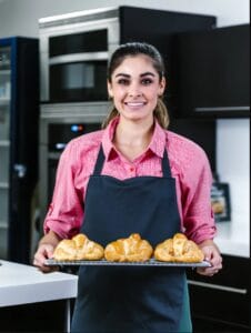 Smiling woman in denim shirt placing tray of croissants into oven