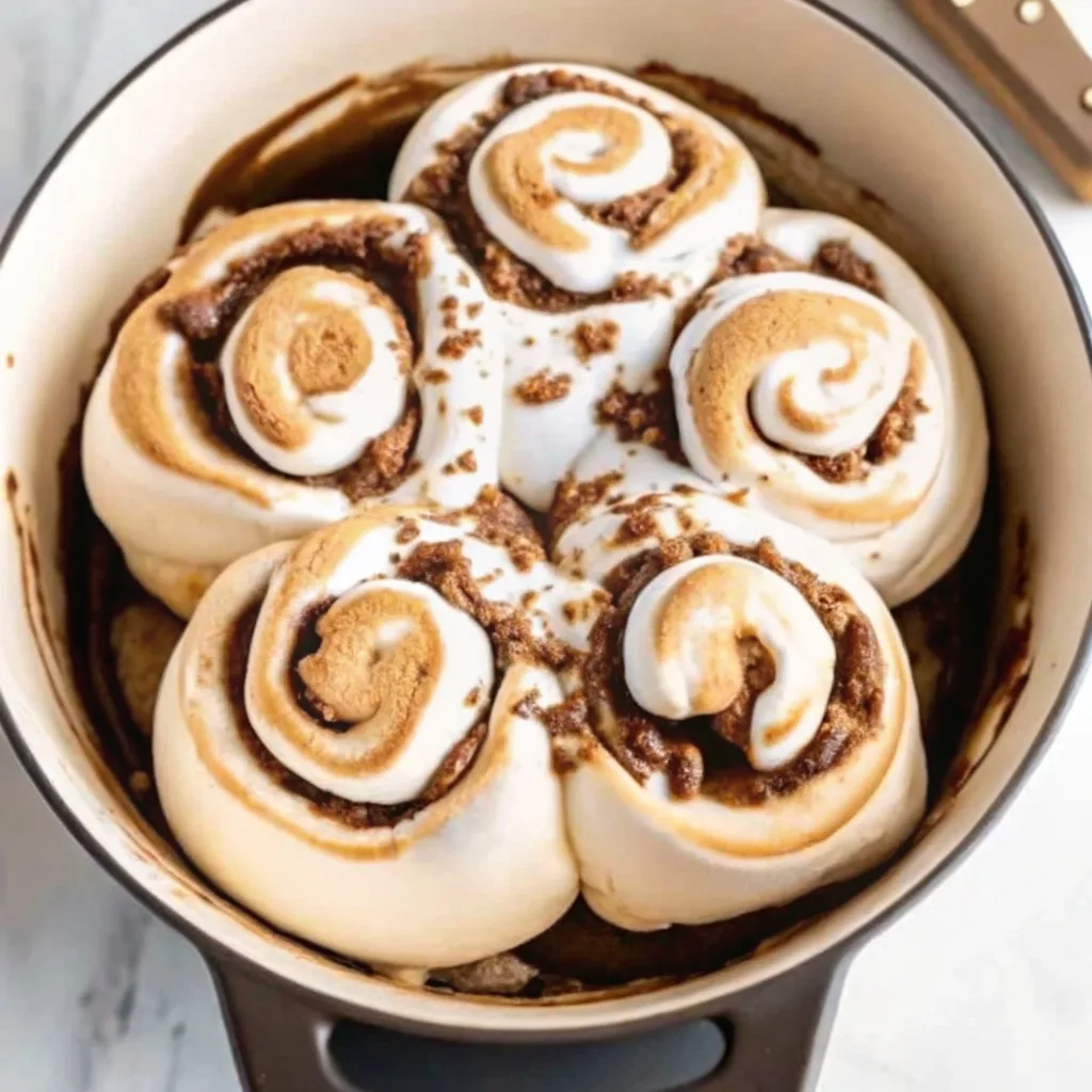 Top view of five large cinnamon rolls in a black cast iron pan topped with thick toasted marshmallow swirls and cinnamon crumble.