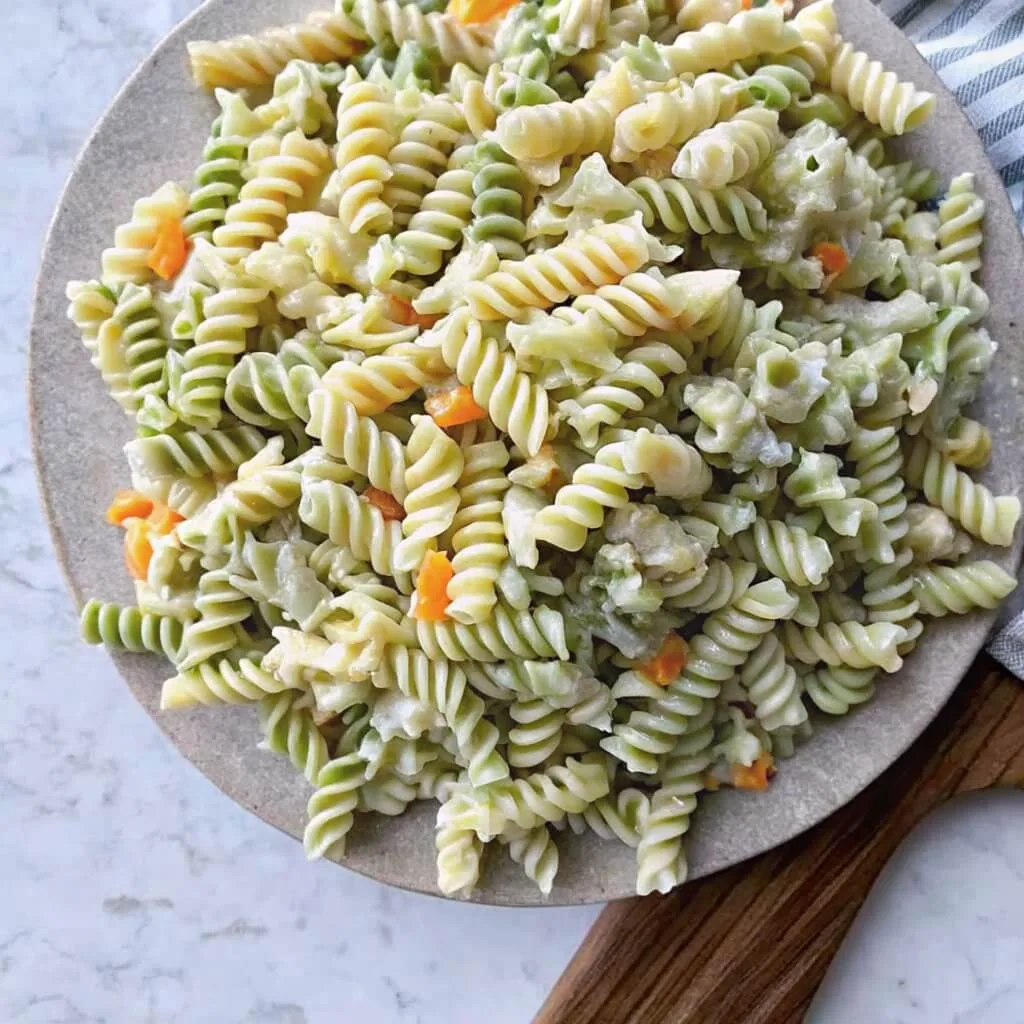 Tri-color pasta salad with green and white rotini, diced carrots, and herb dressing on a round stone plate.