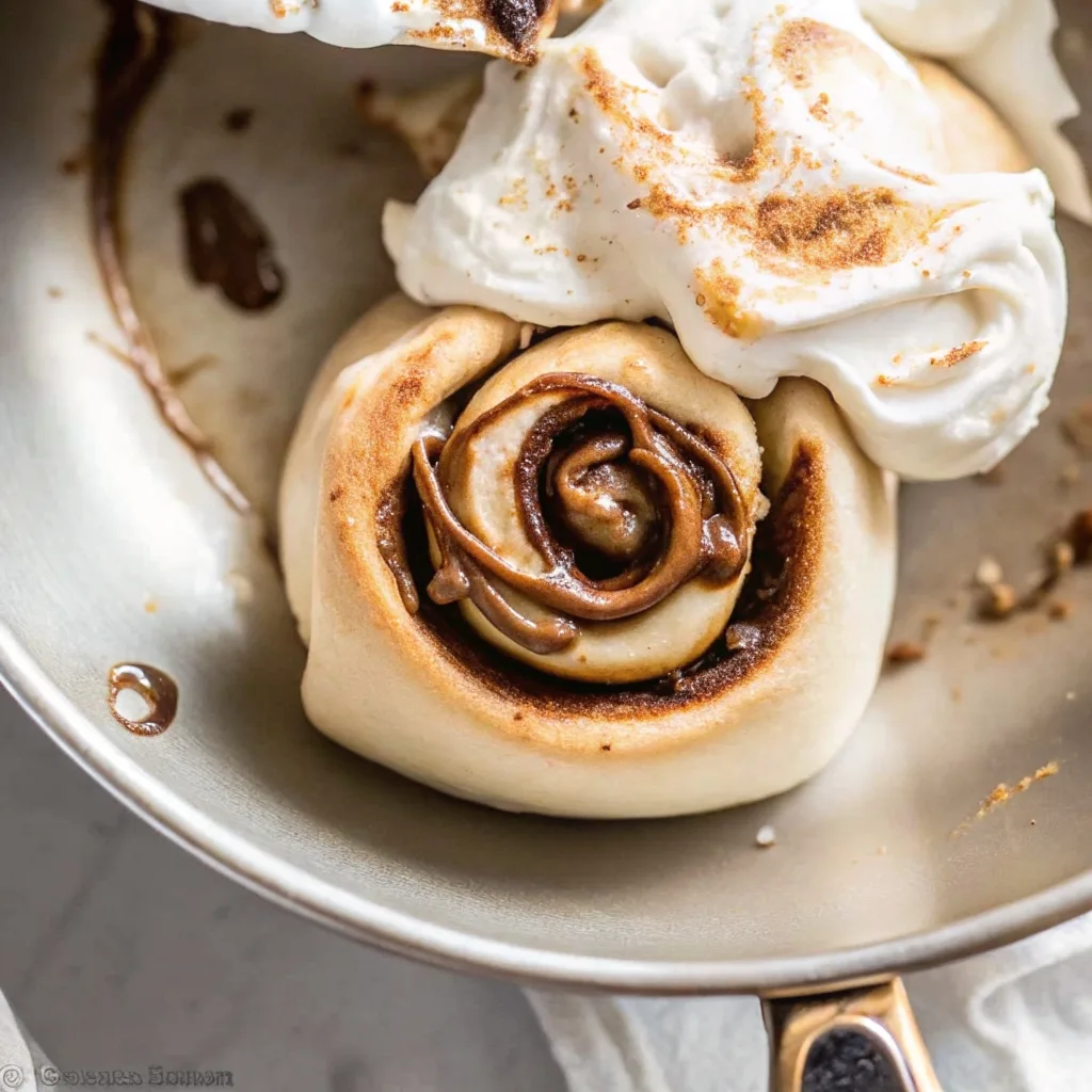 Macro view of a single cinnamon roll in a pan featuring a deep chocolate spiral and a dollop of toasted marshmallow meringue.
