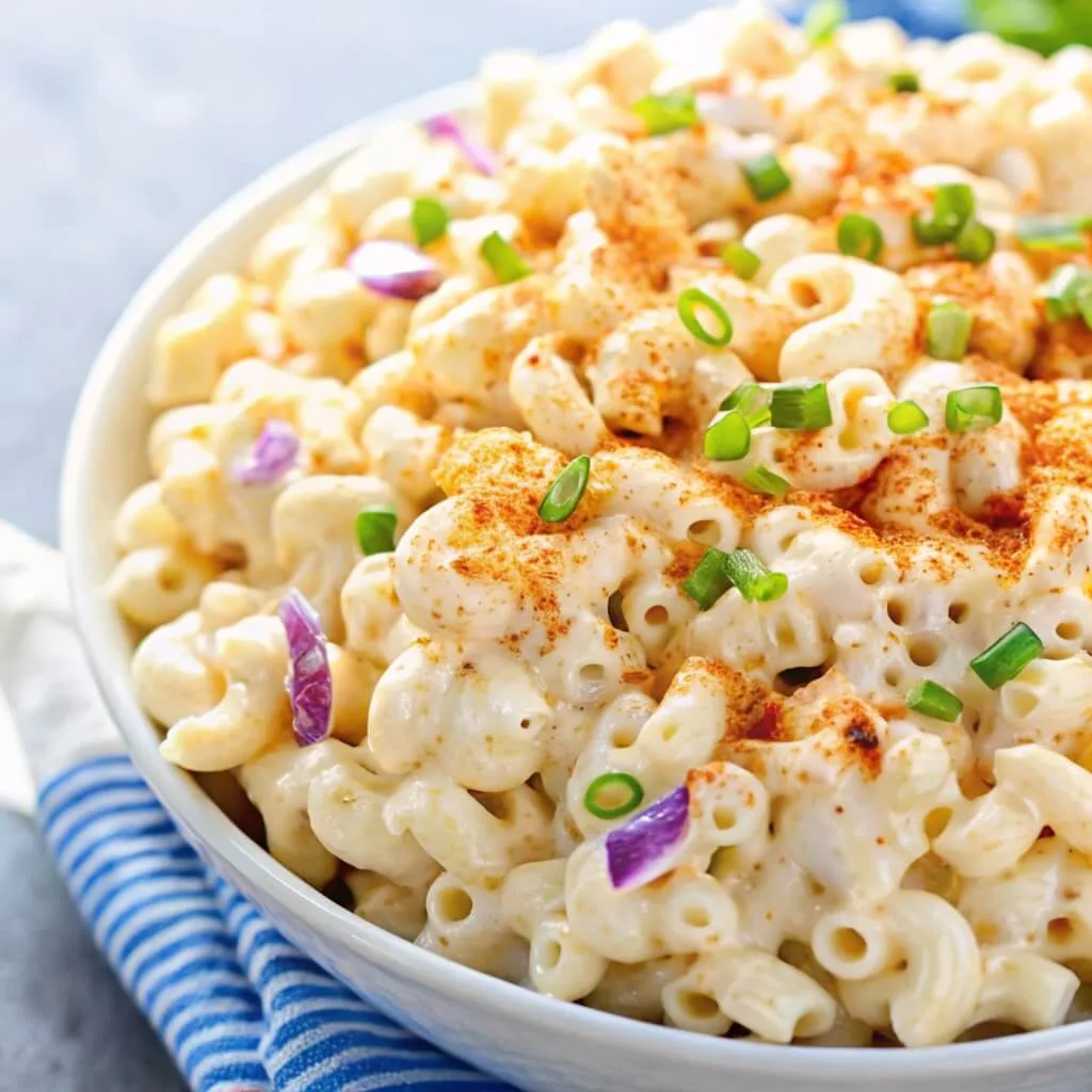 Extreme close-up of individual macaroni noodles coated in creamy dressing with visible pieces of purple onion and chives.