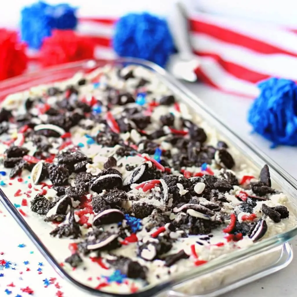 A glass baking dish filled with a patriotic 4th of July dessert topped with crushed Oreo cookies and red and blue sprinkles.