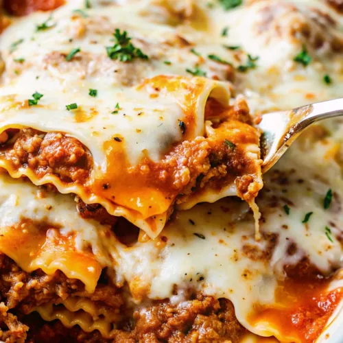 A close-up shot of a silver spatula lifting a cheesy slice of lasagna from a white baking dish, showing layers of pasta, meat sauce, and melted mozzarella.