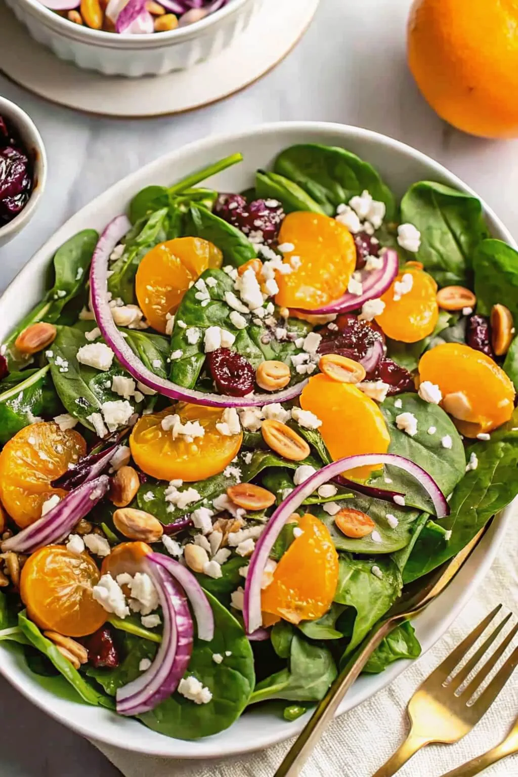 An overhead view of a fresh spinach salad platter topped with mandarin orange slices, red onion rings, feta cheese crumbles, and dried cranberries.