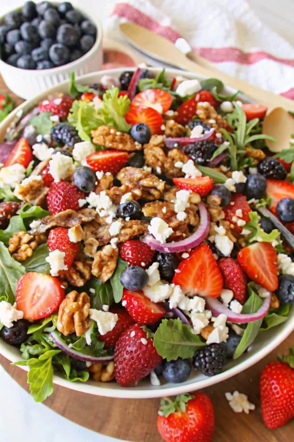 A colorful summer berry spinach salad in a large bowl featuring fresh strawberries, blueberries, blackberries, red onions, walnuts, and crumbled feta cheese.