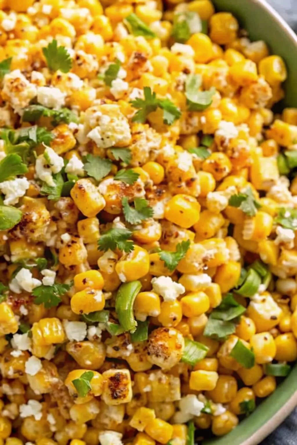 A vibrant close-up of Mexican street corn salad (Esquites) featuring charred corn kernels, crumbled cotija cheese, fresh cilantro, and chili lime seasoning.