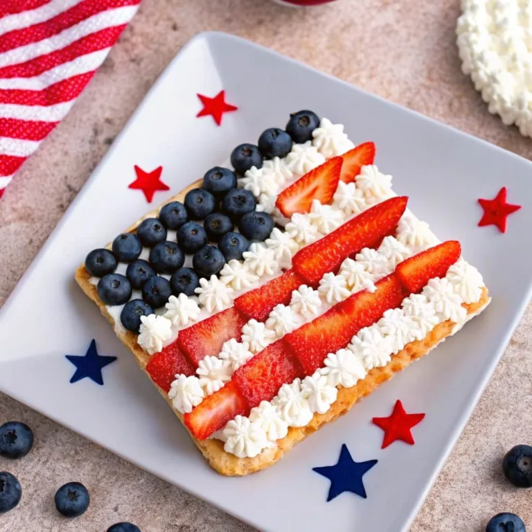 A rectangular shortbread tart decorated with blueberries and strawberries to look like the American flag on a square white plate.