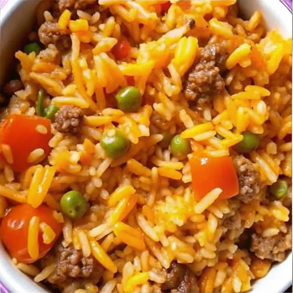 Close up of cheesy taco rice with ground beef, green peas, diced tomatoes, and melted cheddar cheese.
