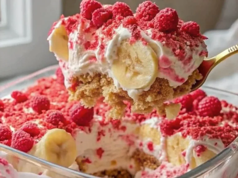 A golden spoon lifting a scoop of no bake raspberry banana icebox cake from a glass dish with whipped cream and fresh fruit.