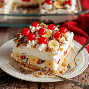 A square slice of no bake banana split dessert lasagna with graham cracker crust, pudding layers, banana slices, and maraschino cherries.