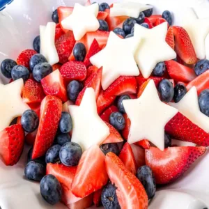 Close up of a patriotic red white and blue fruit salad showcasing juicy sliced strawberries, fresh blueberries, and star-shaped melon or apples.