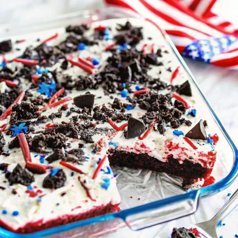 Close-up of a red velvet poke cake with white cream cheese frosting, topped with chocolate cookie crumbles and patriotic sprinkles.