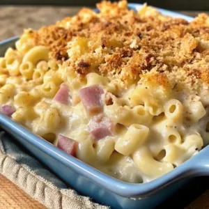A side view of a blue baking dish filled with homemade macaroni and cheese featuring savory protein cubes and a thick, crunchy breadcrumb topping.