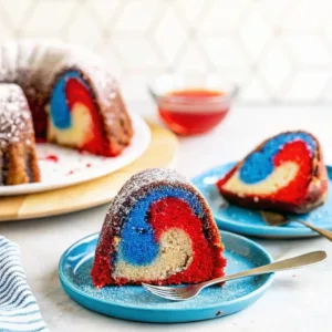 Two individual slices of a red and blue marbled cake on blue plates, with the main bundt cake in the background.