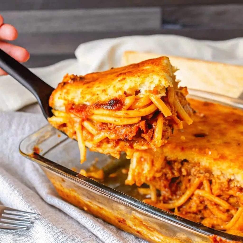 A side profile of a slice of Million Dollar Spaghetti on a spatula, highlighting the thick layers of spaghetti noodles and savory red meat sauce.
