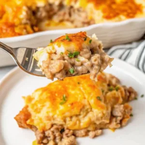 A close-up of a fork holding a bite of cheesy ground beef casserole with a creamy potato topping and fresh herbs.