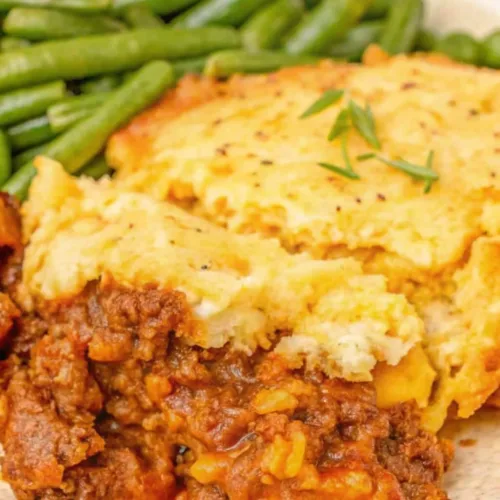 A close-up shot of a plated serving of Shepherd's Pie showing the hearty ground beef filling and a thick, creamy mashed potato and cheese topping.