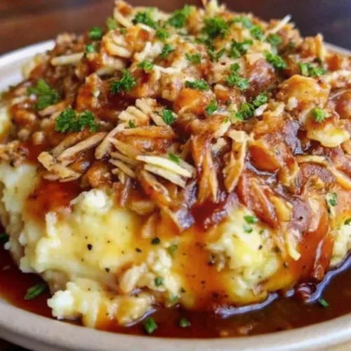 Shredded chicken mashed potato bowl with rich brown gravy and fresh parsley garnish on a plate.