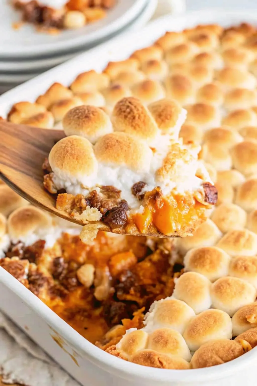 A wooden spoon scooping up a serving of southern sweet potato casserole topped with melted marshmallows.