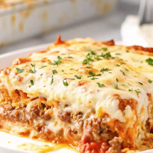 A thick square slice of meat lasagna topped with a bubbly golden cheese crust and fresh parsley on a plate.