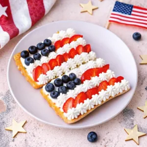 Two flag tarts on a white plate, featuring small white star-shaped icing details on top of the blueberries.