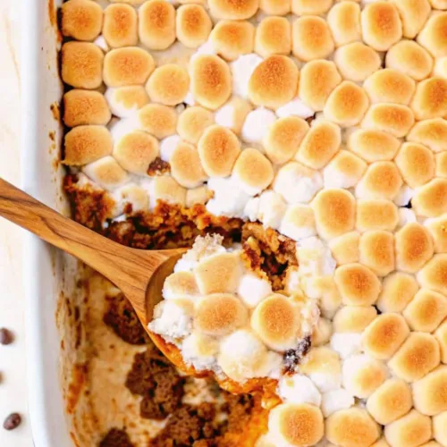 Overhead view of a wooden spoon scooping a portion of sweet potato casserole with toasted marshmallows.