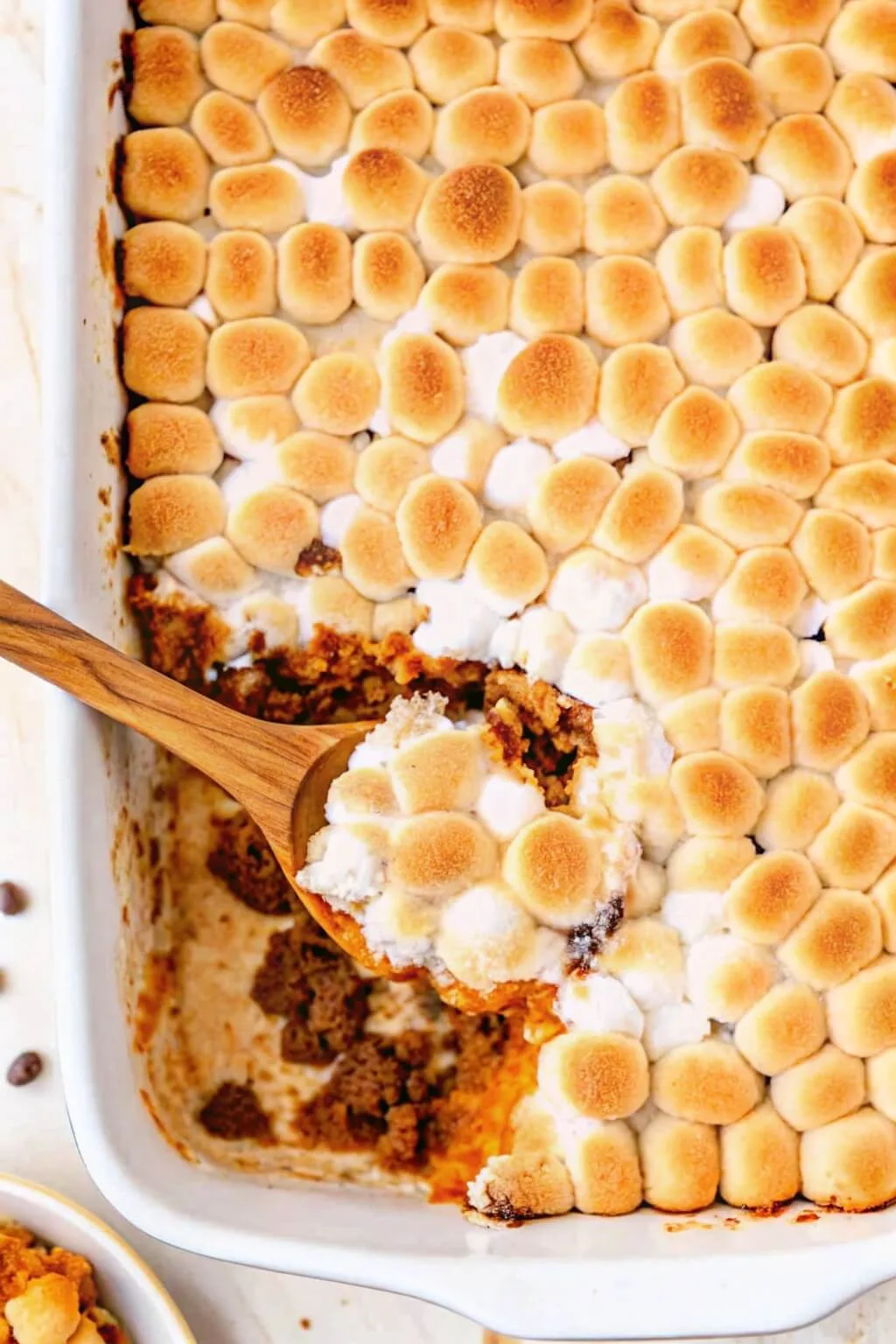 Overhead view of a wooden spoon scooping a portion of sweet potato casserole with toasted marshmallows.