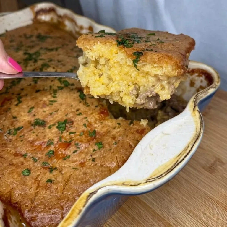 A metal spatula lifting a slice of easy cheeseburger cornbread casserole from a blue baking dish, showing a seasoned ground beef and yellow cornbread filling.