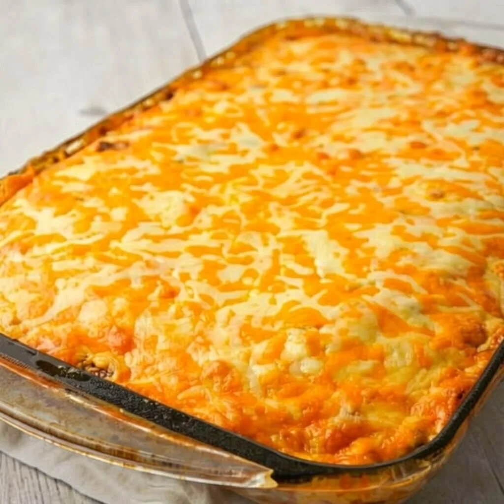 A large glass baking dish filled with an easy Mexican cornbread casserole topped with a thick layer of melted cheddar and Monterey jack cheese.