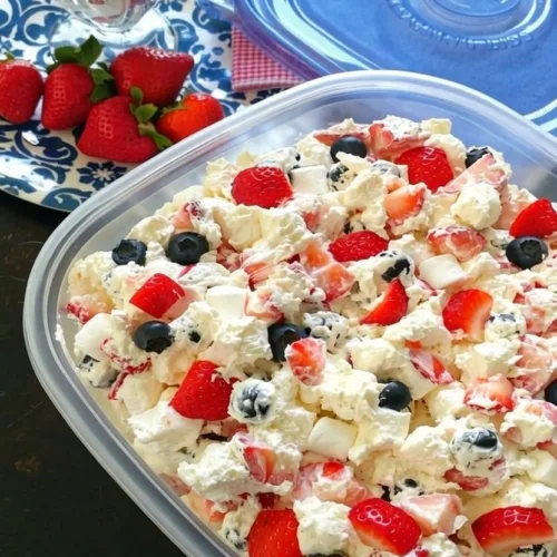 An easy red white and blue berry fluff salad in a clear plastic container, loaded with fresh strawberries, blueberries, mini marshmallows, and whipped cream.