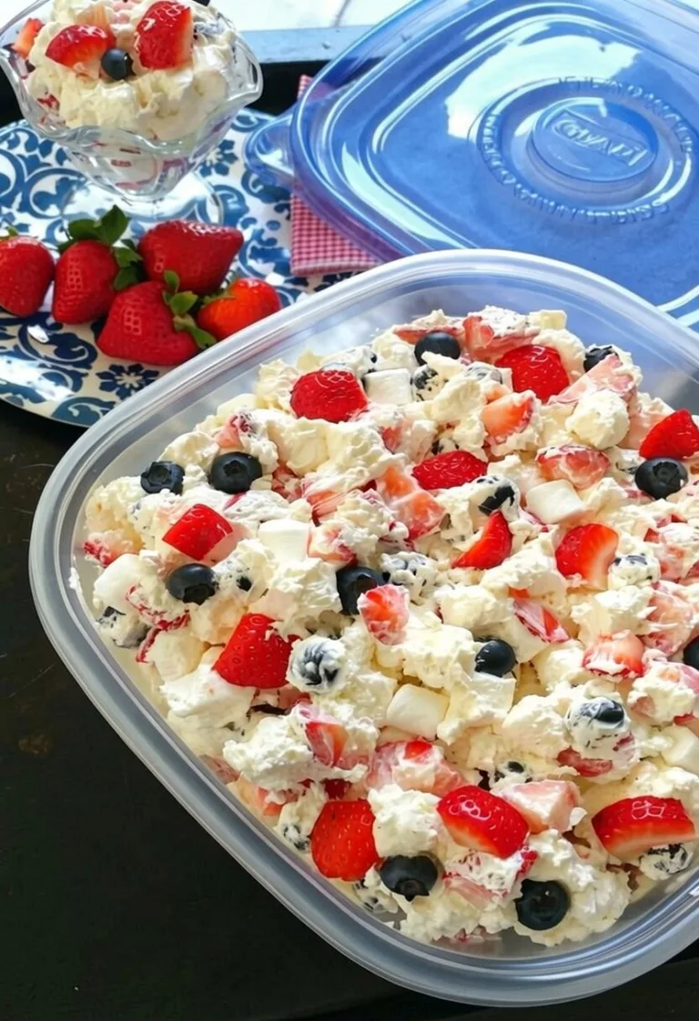 An easy red white and blue berry fluff salad in a clear plastic container, loaded with fresh strawberries, blueberries, mini marshmallows, and whipped cream.