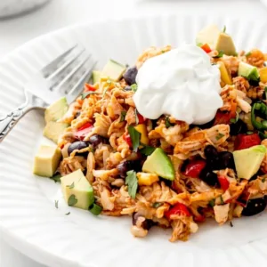 A close up individual serving of an easy Southwest chicken rice casserole on a white plate, topped with fresh avocado cubes and a dollop of sour cream.