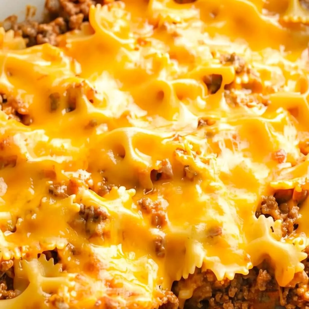 A close up macro shot of an easy cheesy beef pasta bake with melted cheddar cheese covering bowtie pasta and seasoned ground beef.