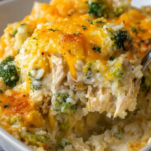 A large spoon lifting a serving of an easy chicken broccoli rice casserole with shredded chicken, broccoli florets, and melted cheddar cheese.