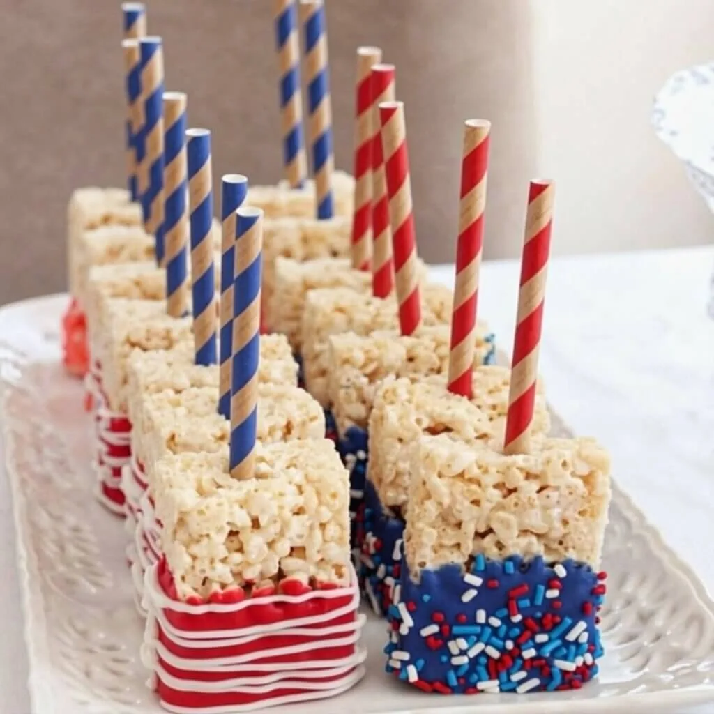 Easy 4th of July rice krispie treats decorated with red, white, and blue chocolate coating and sprinkles, served on paper straws.