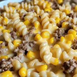 An angled close up shot of a ground beef rotini casserole showing spiral noodles coated in a rich cheese sauce with sweet corn.