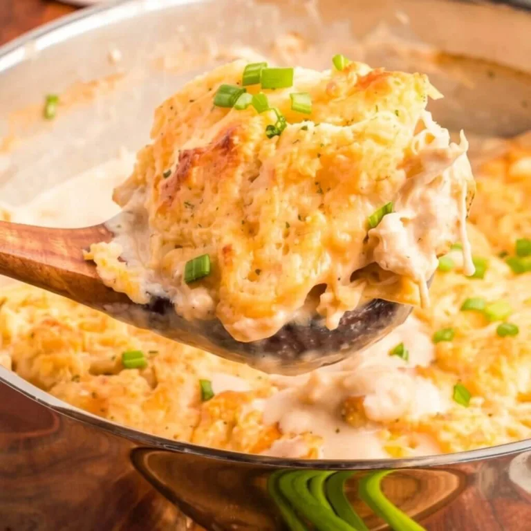 A wooden spoon scooping a portion of a creamy chicken bubble up bake from a stainless steel pan, showing chunks of chicken and gravy.