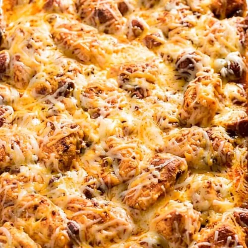 A wooden spoon scooping a portion of a cheesy biscuit pull apart bake with savory meat sauce and melted mozzarella cheese from a glass dish.