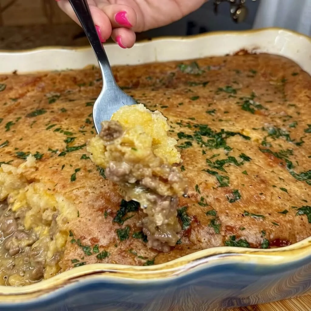 A fork lifting a bite of a jiffy cornbread taco bake directly from a blue ceramic baking dish, highlighting the moist texture.